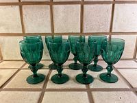 Nine emerald green goblets grouped on tiled counter