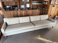 Full view of beige mid-century sofa with wooden legs