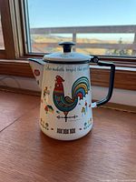 Front view showing rooster design, slogan, handle, spout