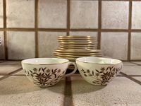 Two teacups and stack of plates showing pattern and gold rim