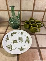 Group shot of Herb Garden plate, hand-blown bottle, and four green mugs