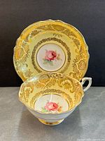 Teacup displayed in front of saucer showing yellow ground, gold filigree and floral centres