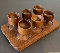 Six teak egg cups positioned in recesses on tray