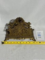 Front view of brass letter holder showing scrollwork and width tape measure