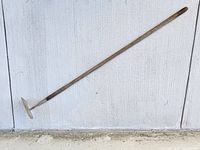 Full view of hoe leaned against white wall showing blade and entire handle