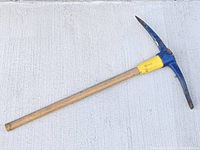 Full view of pickaxe lying on concrete showing head, collar and full handle