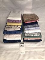 Stack of 19 folded fabric pieces in various colors and prints with MaxSold tag 107