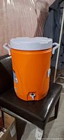 Front view of orange Rubbermaid insulated cooler with lid, spigot and handles visible