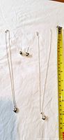 Two necklaces with heart pendants and one pair of heart dangle earrings alongside a tape measure