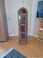 Full view of tall narrow wood cabinet with glass door and side panels