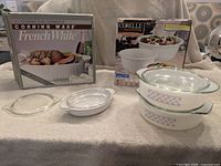 Group shot showing boxed French White casserole, boxed Corelle bowl set, two round casseroles with lids, small oval casserole with lid, and extra lid