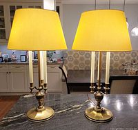 Both brass-tone bouillotte lamps illuminated on countertop with cream shades