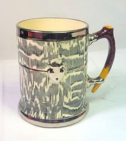 Front view of ceramic tankard showing shield motif, silver bands, branch handle