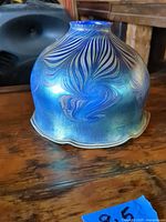 Side view of iridescent blue glass lampshade showing feather swirl pattern and scalloped bottom edge