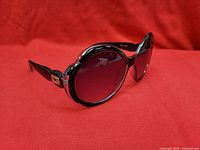 Three-quarter view of black oversized oval Gucci sunglasses on red backdrop