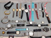 Full overview of 27 assorted wristwatches laid out on table