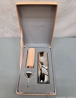 Open box showing perfume bottle, sleeve, funnel in foam insert