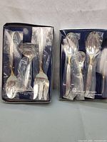 Both boxed Heritage Silversmiths utensil sets side by side