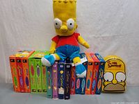 Full lot view with Bart plush sitting on VHS tapes and Homer tin at right
