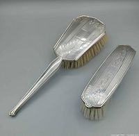 Backs of handled hair brush and oblong clothes brush showing engraved sterling pattern