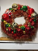 Full view of wreath showing tinsel wrap, assorted bells, ornaments, Santa figure and ruler indicating size