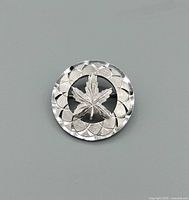 front view of circular sterling brooch with maple leaf and patterned border