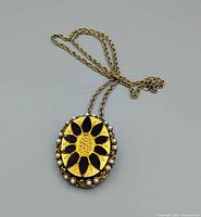 Front view of gold-tone brooch pendant with black petals and faux pearl border attached to chain