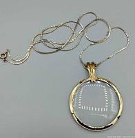 Gold-tone chain and round magnifier pendant laid out
