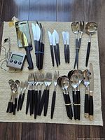 Full set laid out on mat: flatware, serving utensils, kitchen knives, thermometer