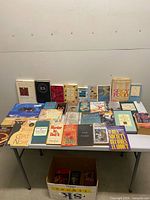 Overall view of table with approximately forty books and box below