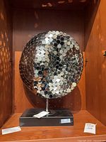 Front view of chrome disc sculpture showing reflective surface and base