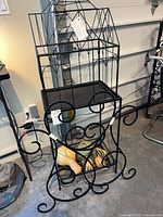 Full view of metal bird-cage plant holder on stand with trellis visible