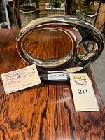 Front view of polished steel abstract sculpture on wood surface with tags visible