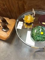 Table top with green glass orb, yellow lotus holder, maroon dish on round glass table
