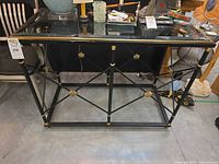Full front view of black and gold metal console table with glass top