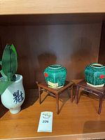 Shelf view showing both green ceramic mini jars on wood stands and white porcelain vase