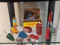 Overall view of lot on shelf showing airplane with box, rocket, telephone booth, gas pump, fire hydrant lighter, spherical toy
