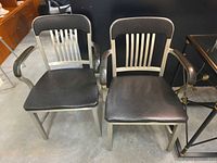 Front view of both steel armchairs with black vinyl seats and backs