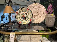Round Imari-style plate and pink chintz scalloped platter displayed on stands