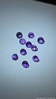 Top view of ten round purple amethyst gemstones on light surface
