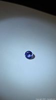 Full view of round diamond-cut tanzanite on neutral background