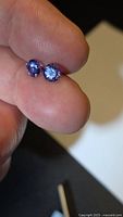 Two round violet-blue tanzanite gemstones held between fingers
