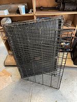 Folded black wire dog crate leaning against shelves