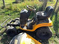 Side view of yellow Poulan Pro riding mower chassis without engine hood, showing seat, steering wheel, rear frame