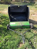 Front view of lawn sweeper showing green housing, brush area and tow bar