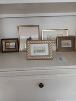 Group of five framed artworks on shelf