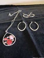 Overview of necklace and two pairs of hoop earrings on black cloth