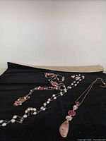 Overall view of the three pink and coral tone necklaces on black background