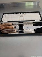 Open case showing knife, fork, honing steel with antler handles in satin and velvet lined box