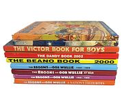 Stack of nine comic annuals showing spines for Victor, Dandy 2002, Beano 2000 and multiple Broons/Oor Wullie titles; Rupert cover on top